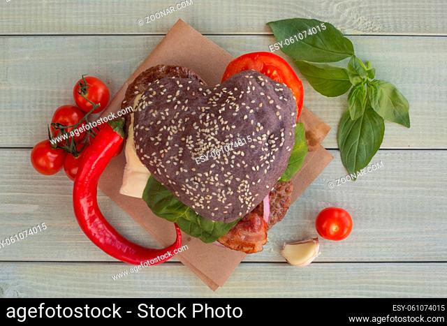 Heart shaped black hamburger and ingredients on wooden background, love burger fast food concept, Valentines day surprise dinner, wooden background