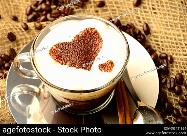 A specialty cup of brewed coffee with a heart shape design while resting among roasted beans