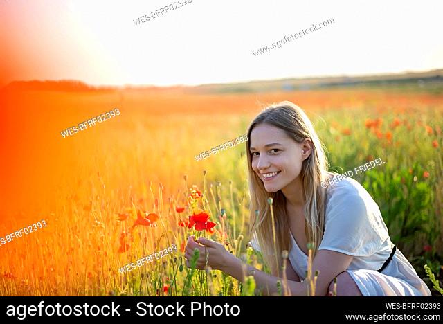 Smiling woman crouching at poppy field