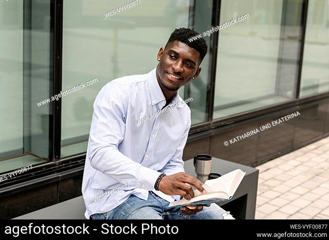 Smiling young man with book sitting on bench