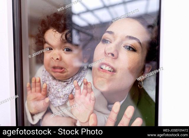 Mother and daughter looking through window pressing faces on glass pane