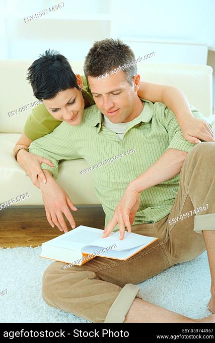 Young couple resting at home couch, reading book, embracing