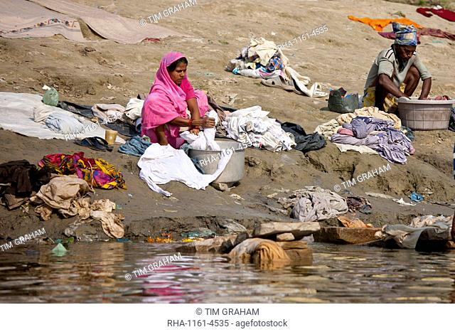 Indian man and woman doing laundry in the waters of The Ganges River at Cabua Pandey Ghat in City of Varanasi, Benares, India