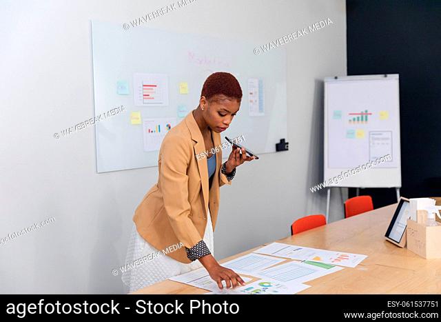 African american young businesswoman talking through smart phone and analyzing charts in office