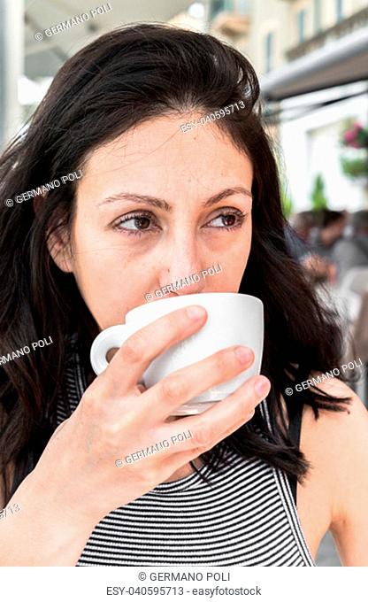Pensive pretty young woman drinking in an outdoor local a beverage. Lifestyle and concepts