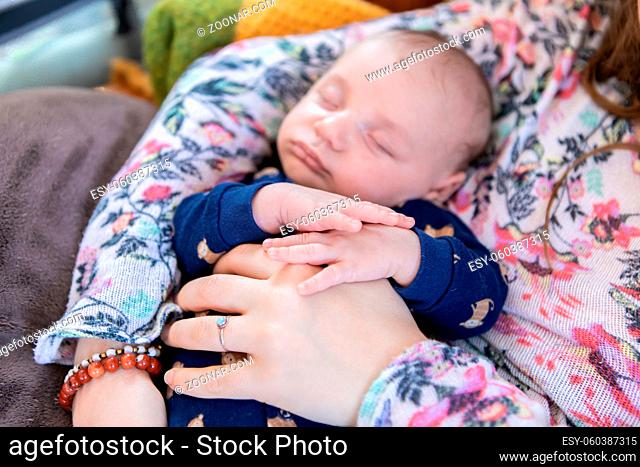 Selective focus shot of an infant boy in his mother's arms. The child's small fingers resting on his mothers hands that hold him protectively