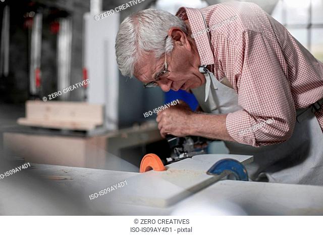 Senior carpenter using jigsaw tool in workshop