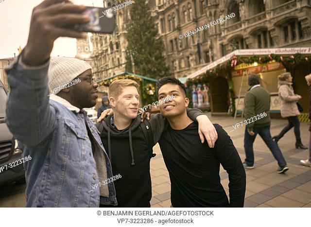 young men taking selfie in front of Neues Rathaus and Christmas market at Marienplatz in Munich, Germany