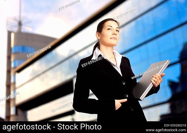 Businesswoman holds a modern laptop in front of an office building