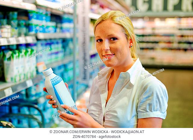 Eine junge Frau kauft Milch im Supermarkt. Steht vor dem Kühlregal