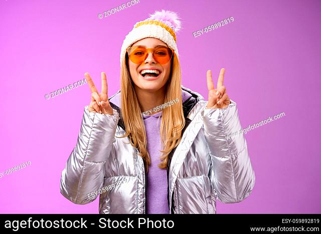 Friendly lucky optimistic beautiful blond woman in sunglasses silver stylish jacket winter hat show peace victory gesture enjoying snowy vacation get outside...