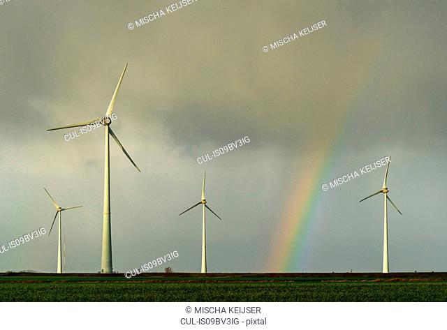 Field landscape with rainbow between turbines on wind farm in north Netherlands, near waddensea dyke
