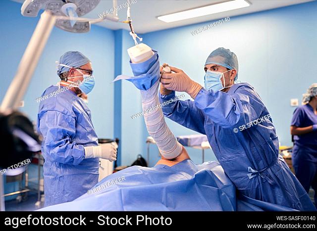 Doctor wrapping hand while standing with colleague in background at operation room