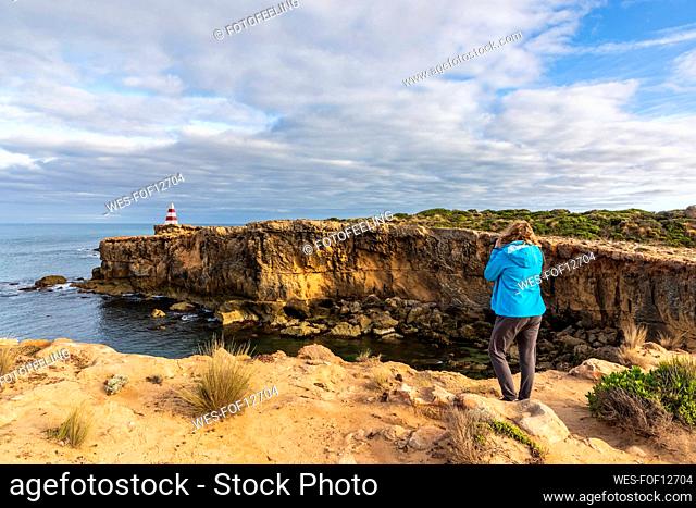 Australia, South Australia, Robe, Female tourist photographing Cape Dombey Obelisk and surrounding cliffs