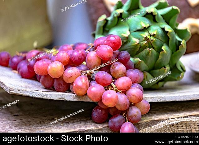 Marktstand mit roten Weintrauben und Artischocke auf einem rustikalem Holzbrett