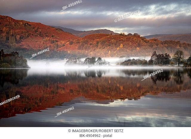 Reflecting water surface at sunrise with fog, hilly landscape, Rydal Water, Ambleside, Lake District National Park, Central England, Great Britain