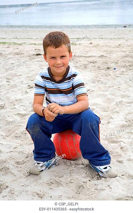 Beautiful boy sitting on a ball on the beach