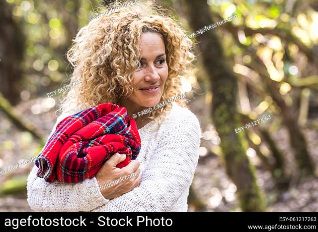 Cheerful woman embrace red warm cover and smile with forest woods trees in background - people and outdoor leisure activity in the wild and beautiful nature