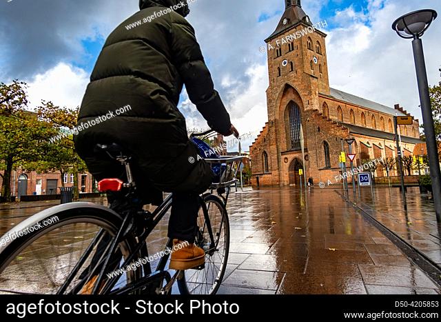 Odense, Denmark A woman bicycles in the rain past the St. Canute's Cathedral, or. Sankt Knuds Kirke