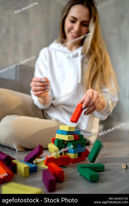 Smiling woman playing with multi colored toy blocks at home
