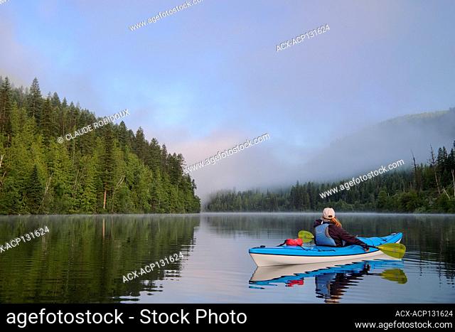 Kayaker with blue kayak on Echo Lake at sunrise, Echo Lake provincial park near Lumby, British Columbia, Canada