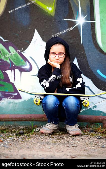 Girl with skateboard against the wall. Child looking at the camera. Vertical shot. Selective focus