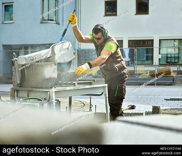 Construction worker cutting paving stone with machinery at site