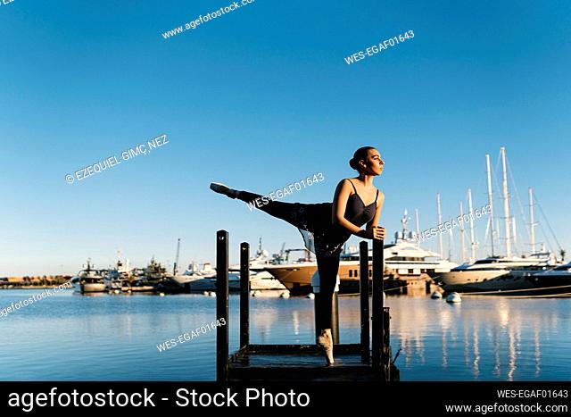Female dancer praciting on jetty while looking away against blue sky