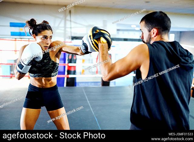 Female boxer sparring with her coach in gym