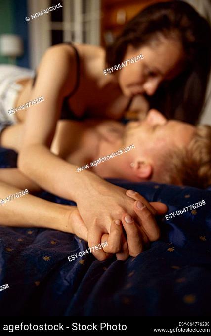 Passionate beautiful couple having sex in bed. Focus on hands folded together. Intimate relationship concept