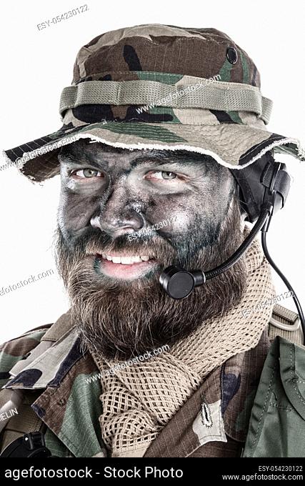 Shoulder studio portrait of commando soldier, modern mercenary, professional soldier with black camouflage paint on bearded face
