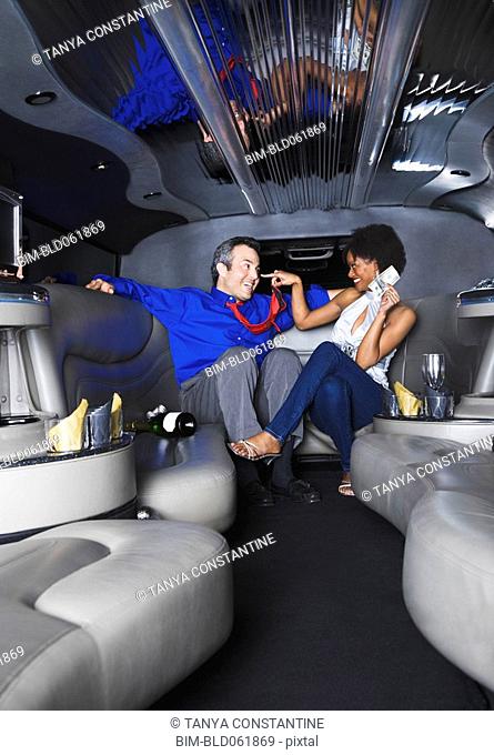 Multi-ethnic couple in with champagne and money in limousine
