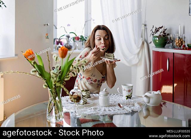 Happy woman eating slice of cake sitting at dining table