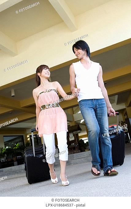 Young couple carrying suitcases, smiling, Saipan, USA