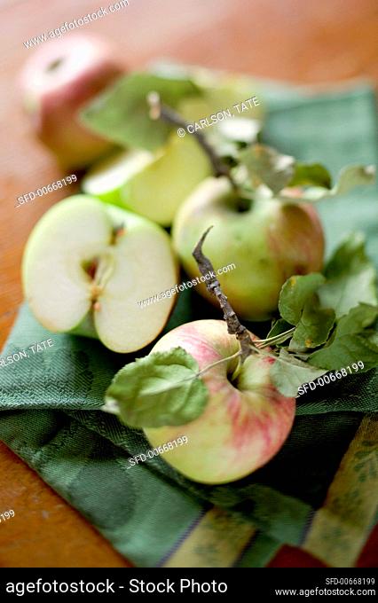 Whole and half apples with leaves on tea towel