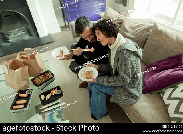 Affectionate couple enjoying takeout food with chopsticks on sofa