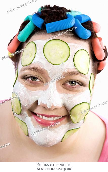 Portrait of smiling woman wearing curlers and beauty mask with slices of cucumber
