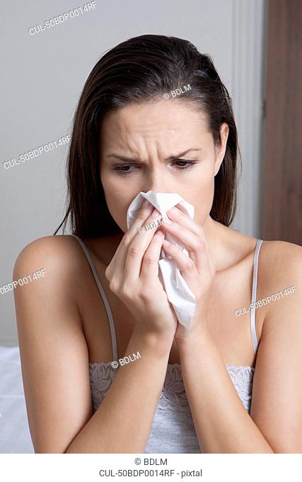 Woman blowing her nose on bed