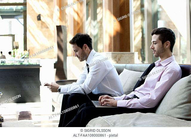 Businessmen using wireless devices in waiting room