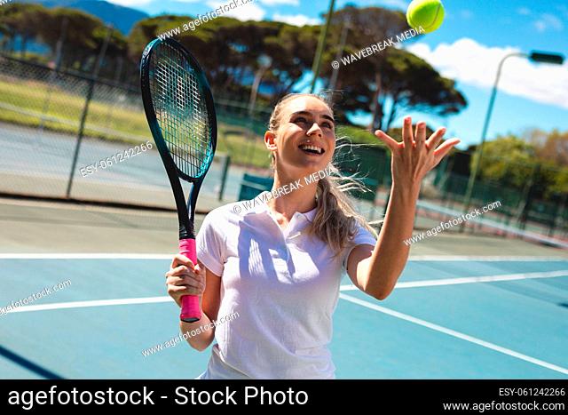 Cheerful young caucasian female player holding tennis racket while catching ball at court