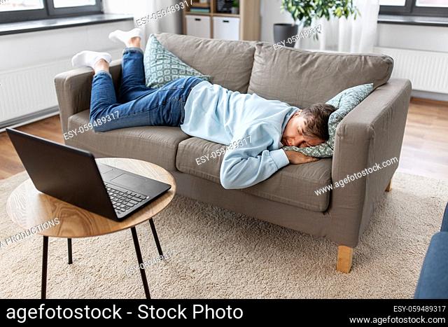 bored man with laptop lying on sofa at home