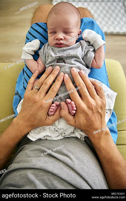 Overhead shot of father's hands resting on sleeping three month old baby boy wearing mittens
