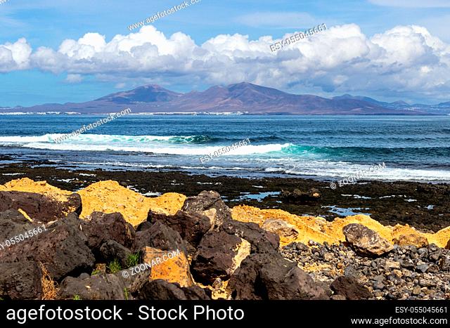 Panoramic view at the coastline of Corralejo on canary island Fuerteventura, Spain with lava rocks and rough sea with waves and canary island Lanzarote in the...