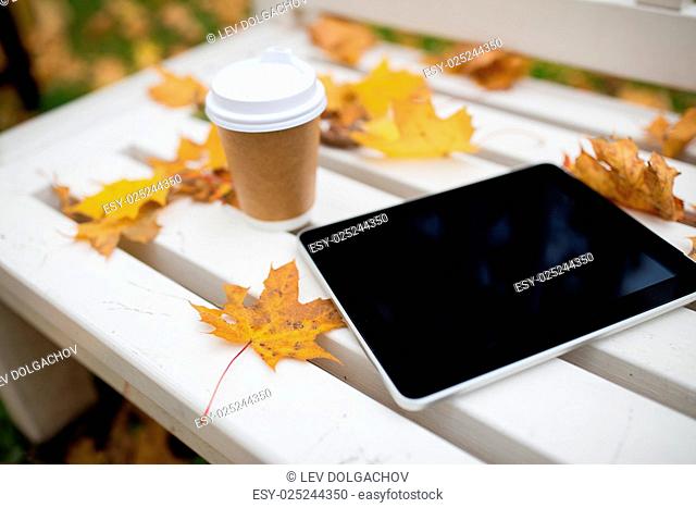 season, technology and advertisement concept - tablet pc computer and coffee paper cup on bench in autumn park
