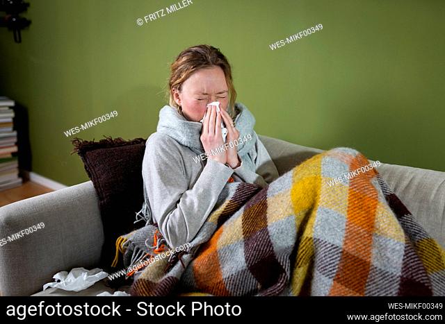 Sick young woman sneezing in tissue relaxing on couch