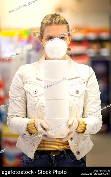 Teenage girl wearing protectice mask and gloves holding stack of four toilet rolls at supermarket