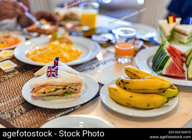 Healthy Breakfast Concept. Club Sandwich presented with English Flag on top along with fruits and juice at breakfast table