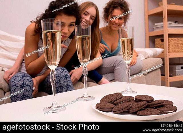 Three young girls making pajamas party. Enjoying with champagne and cookies