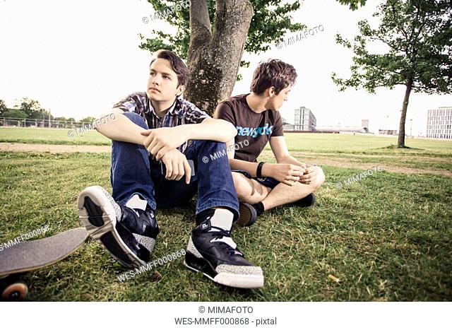 Germany, Berlin, two teenage boys in bad mood sitting under a tree