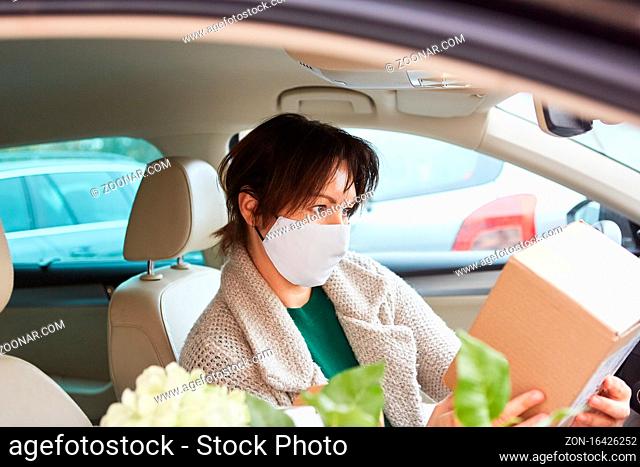 Frau mit Mundschutz prüft Paket nach Abholung oder vor Übergabe im Innenraum ihres Autos